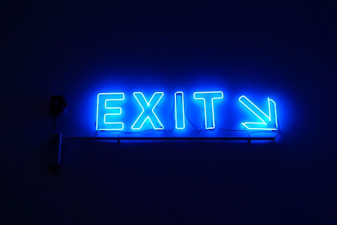 The image features a glowing neon blue sign that clearly states 'EXIT' with an arrow pointing to the right. The backdrop is dark, highlighting the brightness of the neon lighting.