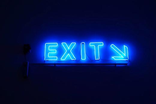 The image features a glowing neon blue sign that clearly states 'EXIT' with an arrow pointing to the right. The backdrop is dark, highlighting the brightness of the neon lighting.