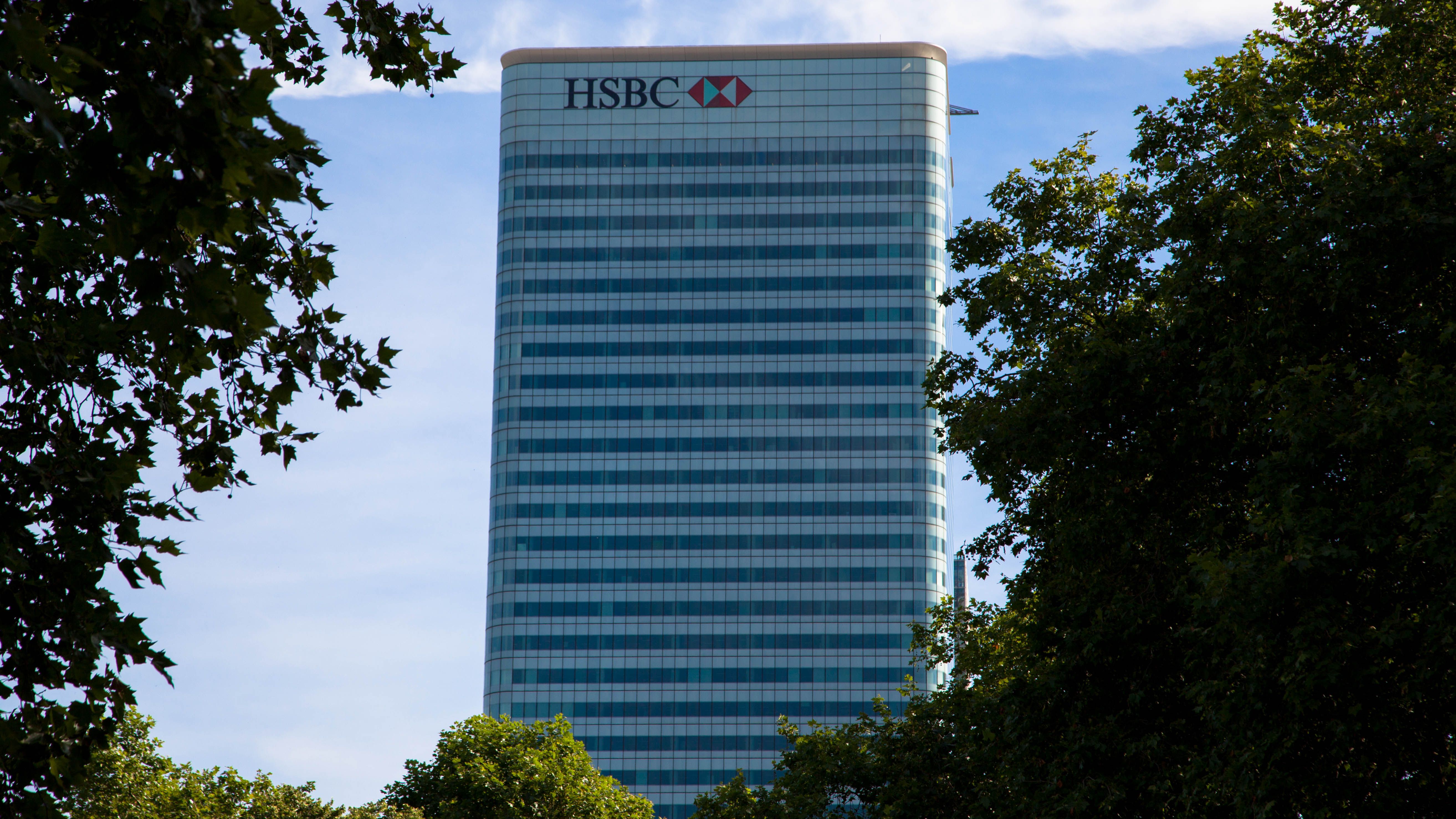 The image features a tall glass building with the HSBC logo prominently displayed at the top. Surrounding the building are trees, creating a natural frame for the financial institution's headquarters.