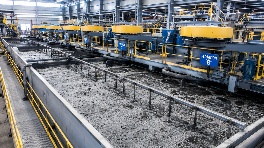 The image depicts a flotation circuit within an industrial facility, showcasing multiple flotation cells processing slurry. The area is characterized by metal walkways and machinery, highlighting the industrial process involved in mineral extraction.