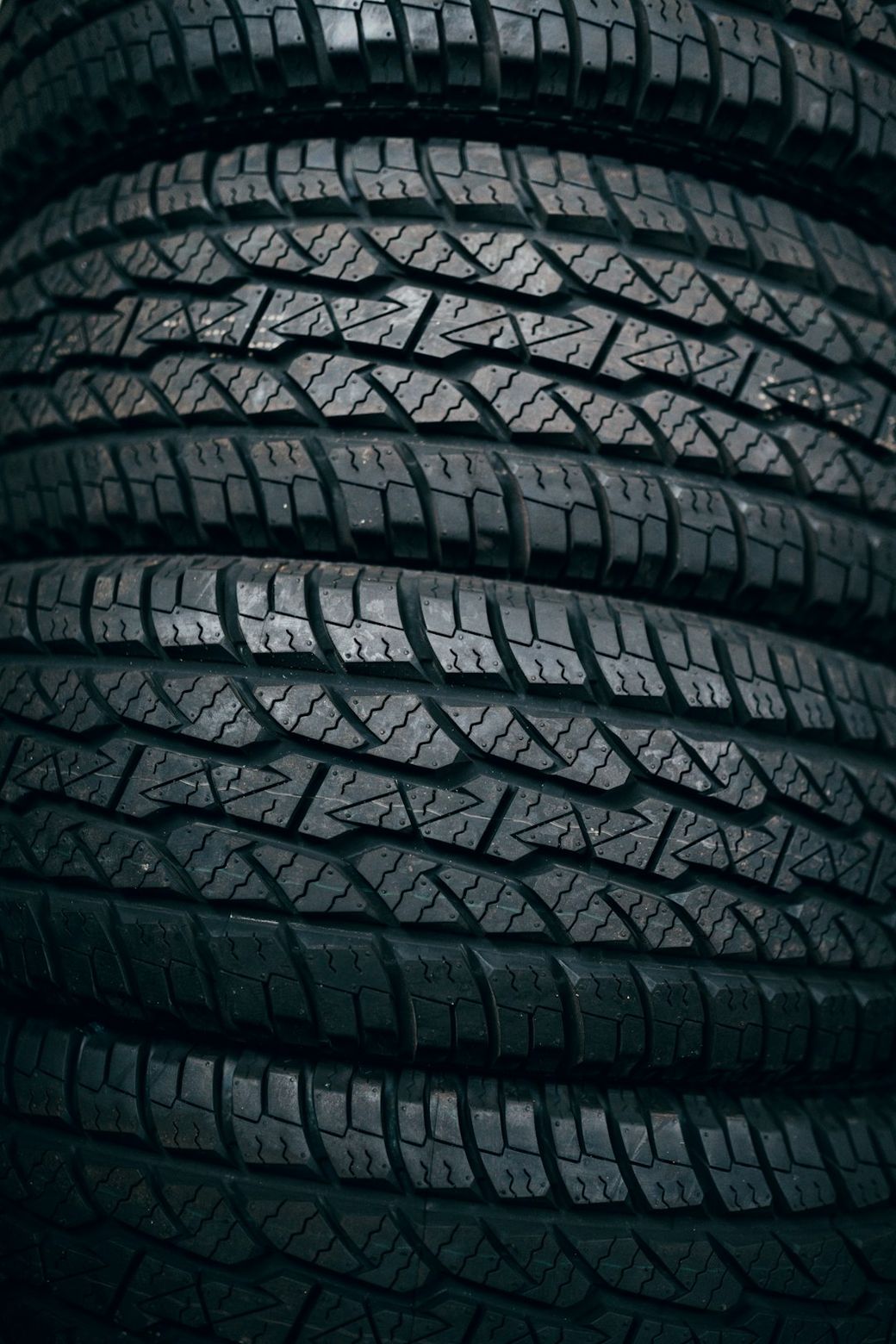 The image features a close-up view of several stacked car tires, showcasing their intricate tread patterns and rubber texture. The composition emphasizes the physical details of the tires, highlighting their readiness for automotive use. — Credit: Photo by Shadrach Warid on Unsplash