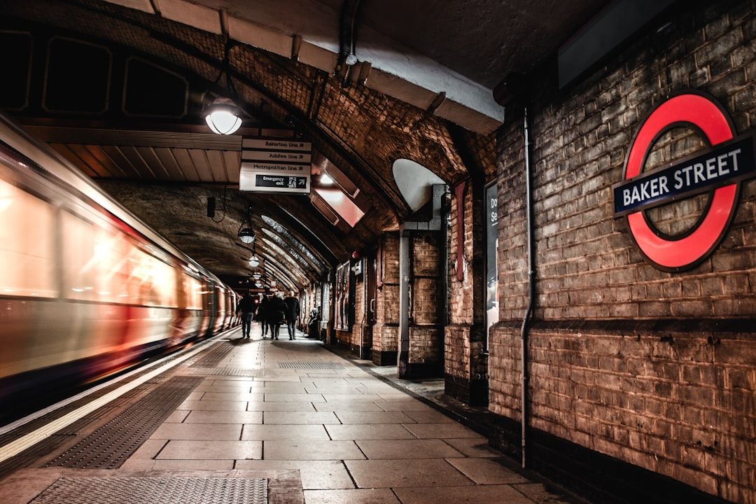 The image depicts a partially blurred scene of the Baker Street underground station in London. The platform is lined with brick walls and features the iconic London Underground roundel sign for Baker Street.