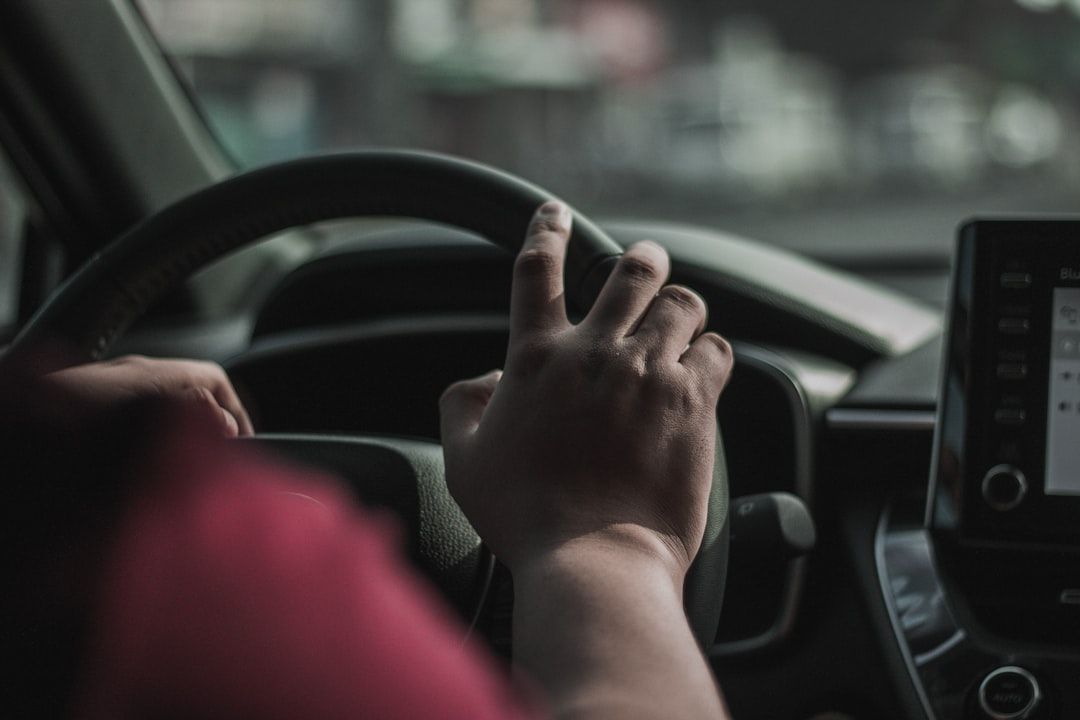 The image shows a close-up view of a person's hand gripping the steering wheel of a car. The interior of the vehicle is partially visible, with a focus on the dashboard.