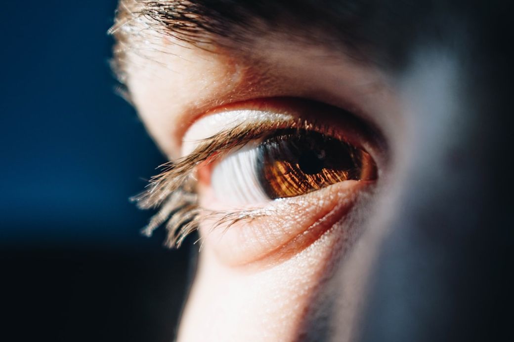 A close-up of a human eye showcasing the intricate details of the iris and eyelashes. The image captures the reflection of light within the eye, highlighting the rich brown color of the iris. — Credit: Photo by Bacila Vlad on Unsplash