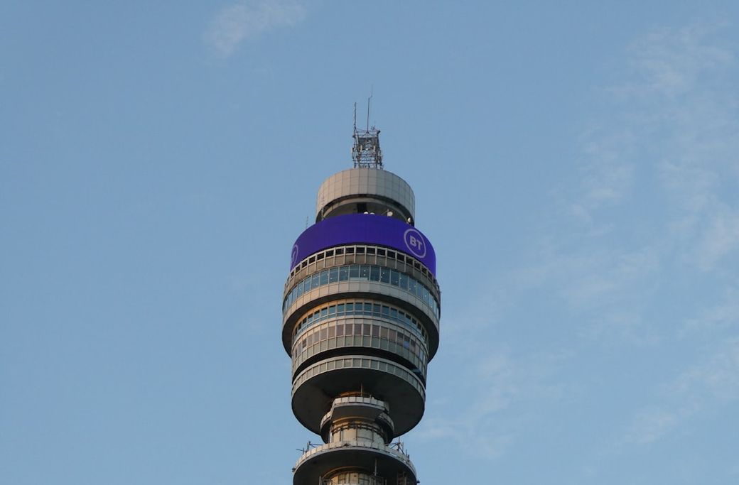 The image features the iconic BT Tower prominently against a clear blue sky. Its distinctive cylindrical shape and observation windows are highlighted, showcasing its architectural design. — Credit: Photo by Seb Doe on Unsplash