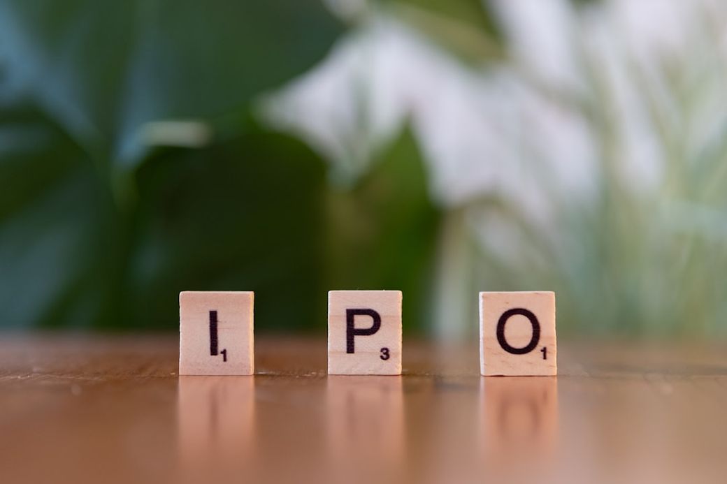 The image shows wooden letter tiles spelling out 'IPO' against a blurred green background. The tiles are positioned on a wooden surface, suggesting a focus on finance or investment themes. — Credit: Photo by Markus Winkler on Unsplash