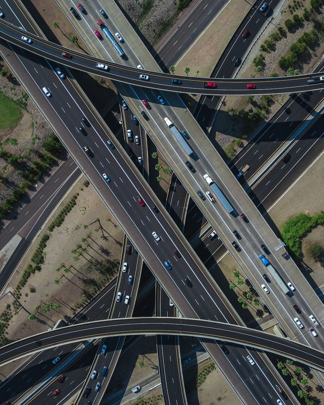 An aerial view of a complex highway interchange showing multiple levels of roads and vehicles. The image captures the intricate design of the road network, illustrating the flow of traffic and surrounding landscape. — Credit: Photo by Jared Murray on Unsplash