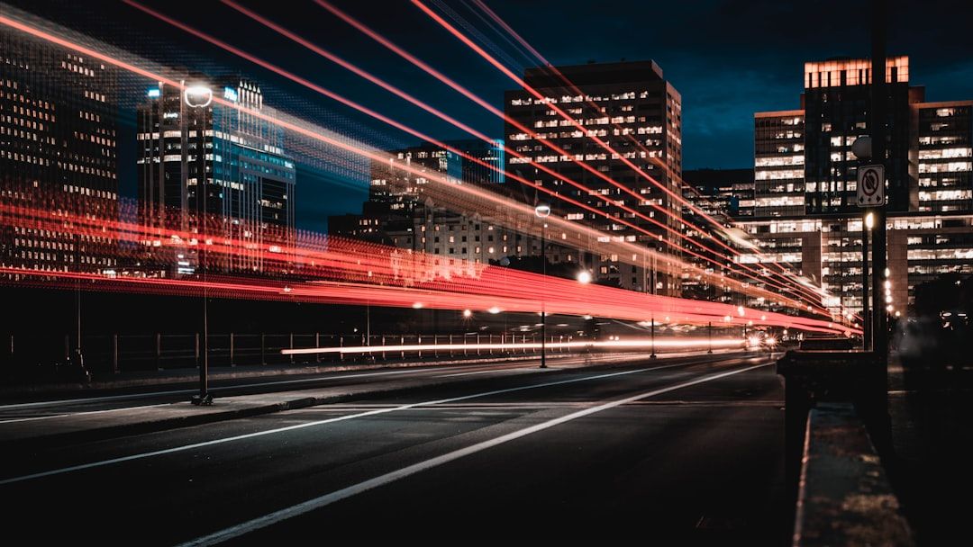 A cityscape at night featuring blurred light trails that suggest motion, with skyscrapers illuminated in the background. The image captures a sense of urban life and the dynamic nature of a city after dark.