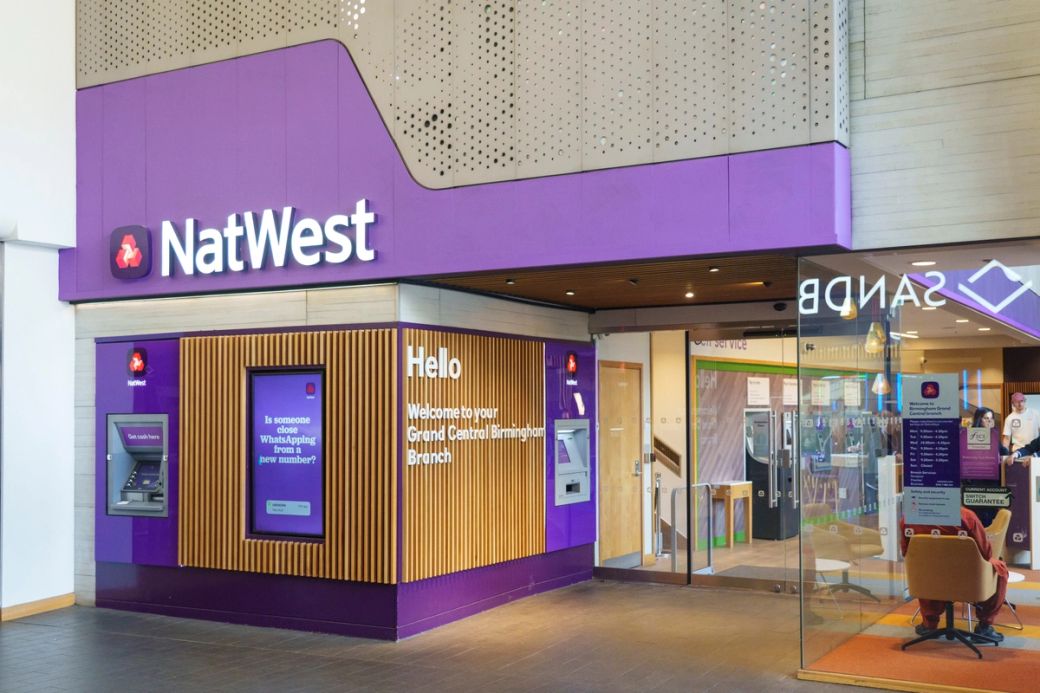 The image shows the exterior of a NatWest bank branch, featuring a modern design with a purple color scheme. An ATM is visible alongside signage welcoming customers to the location. — Credit: Dominic Lipinski/NatWest Group
