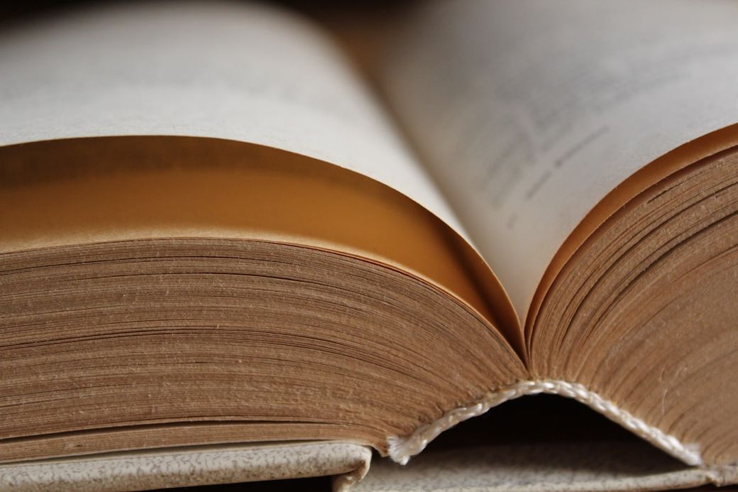An open book is shown, displaying its pages curling towards the center. The focus is on the spine and the texture of the pages, highlighting their worn and aged appearance. — Credit: Photo by Ali Alauda on Unsplash