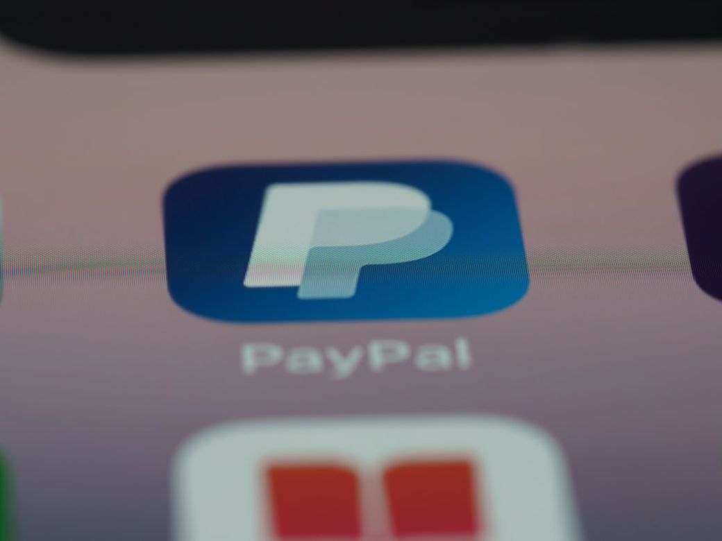 The image features a close-up view of a smartphone screen displaying the PayPal app icon. The logo is prominently featured against a blurred background, emphasizing digital finance and payment technology. — Credit: Photo by Brett Jordan on Unsplash