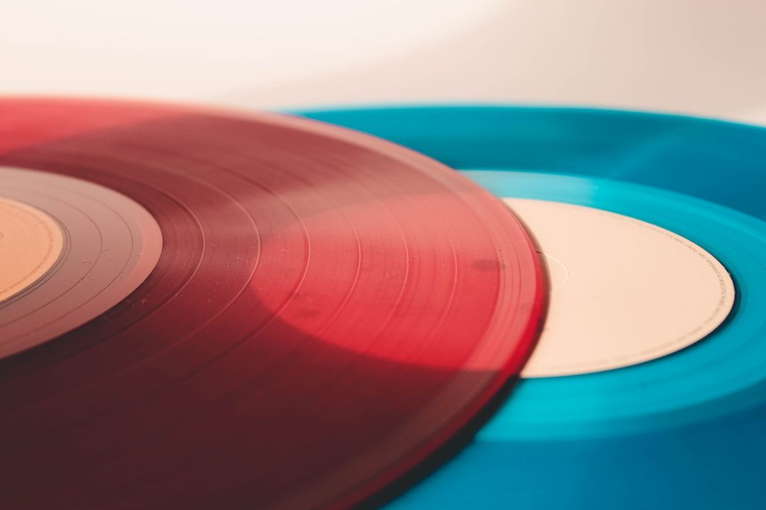 The image features two vinyl records overlapping each other, one in a deep red hue and the other in a bright blue shade. The background is light and neutral, highlighting the colors of the records.