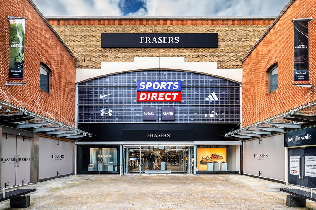 The image shows the exterior of a sports retail store named 'Frasers'. Prominent brands displayed include Nike, Adidas, Under Armour, Puma, and others within the storefront signage.