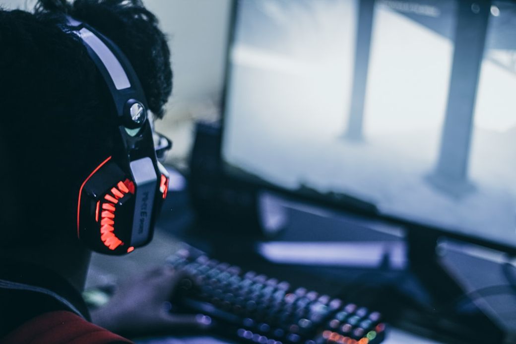 The image features an individual wearing illuminated gaming headphones while engaged in a computer activity. The setting includes a computer screen, suggesting a focus on gaming or digital entertainment. — Credit: Photo by Fredrick Tendong on Unsplash