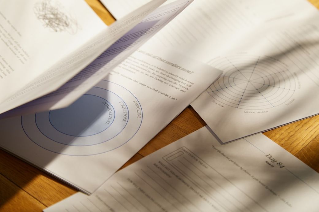The image features a collection of papers scattered on a wooden surface, showcasing various worksheets related to well-being and personal development. Different sections of the papers include diagrams and text prompts for self-reflection. — Credit: Photo by Joonas Sild on Unsplash
