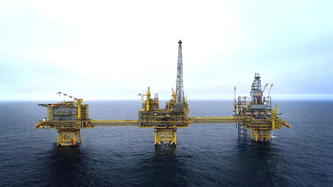 The image depicts an offshore oil rig situated in the open sea. The structure features multiple platforms, cranes, and equipment typically associated with oil extraction.
