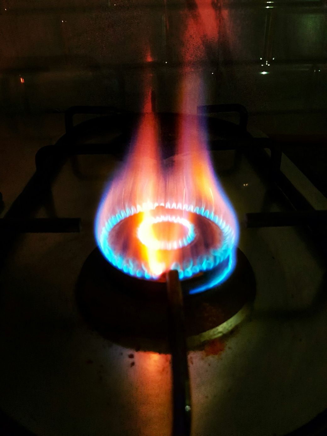 The image depicts a close-up view of a gas burner with a vibrant flame. The flames are blue and orange, creating a visually striking spiral pattern that emanates from the circular burner. — Credit: Photo by Pruthvi Sagar A R on Unsplash