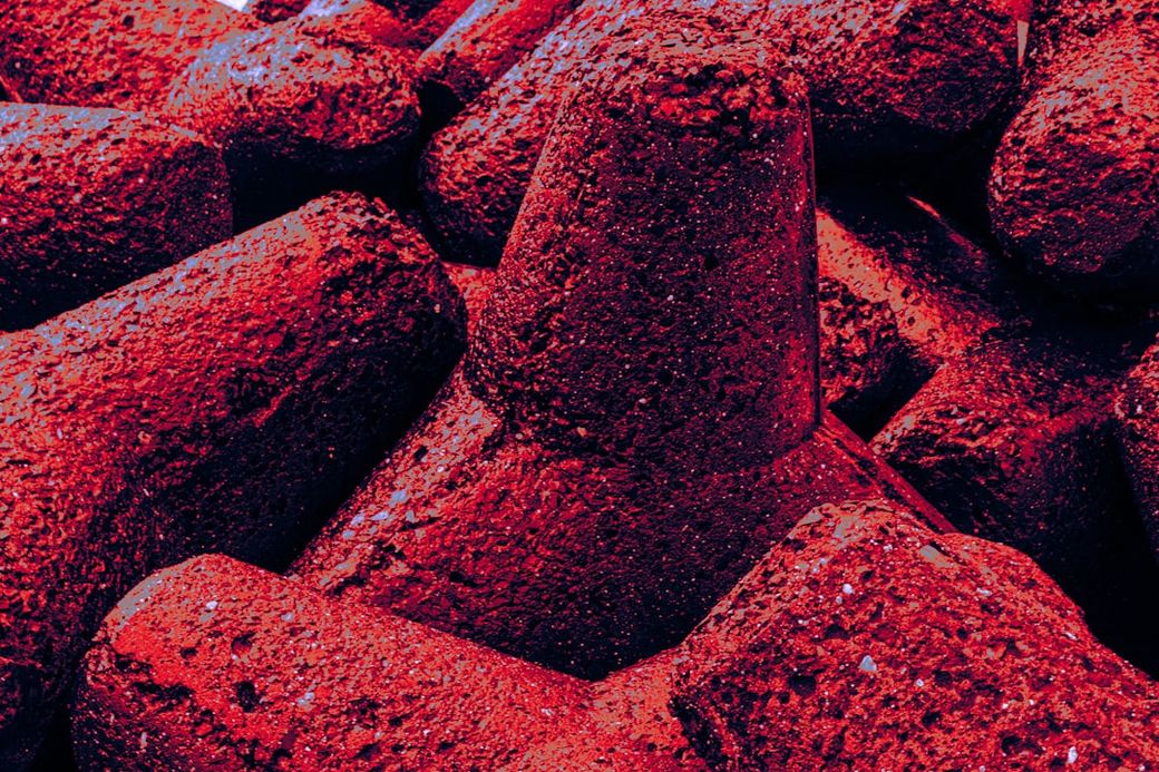 The image features a close-up of several conical objects with a rough texture, predominantly in red hues. The interplay of light and shadow highlights the uneven surfaces of these forms, creating a visually striking composition. — Credit: Photo by Zoshua Colah on Unsplash