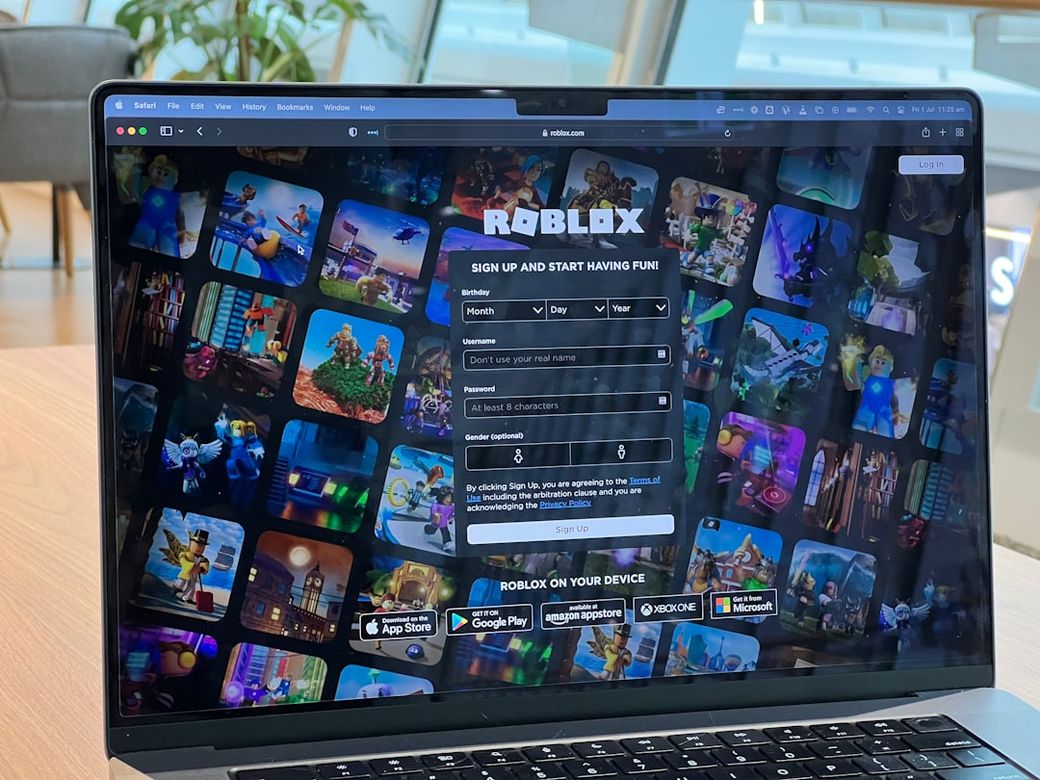 The image shows a laptop screen displaying the Roblox sign-up page. The background features a collage of various game graphics from Roblox, highlighting the platform's diverse offerings. — Credit: Photo by Oberon Copeland @veryinformed.com on Unsplash