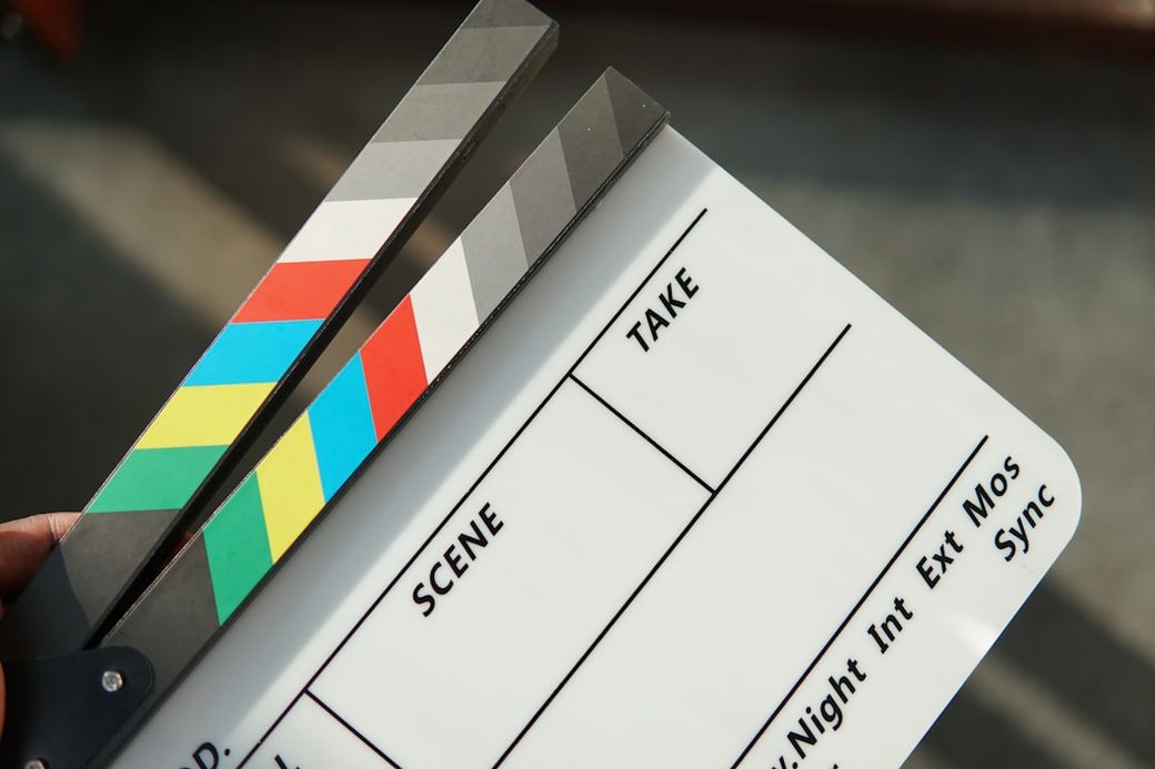 The image features a film clapperboard being held, which is used in movie production to denote the start of a scene. The clapperboard displays sections for 'Scene' and 'Take' information, suggesting it is prepared for filming. — Credit: Photo by Amjith S on Unsplash