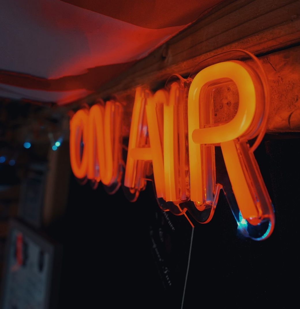 The image features a brightly lit neon sign that reads 'ON AIR'. The sign is prominently displayed in a setting likely related to broadcasting or media production. — Credit: Photo by Alan Findlay on Unsplash