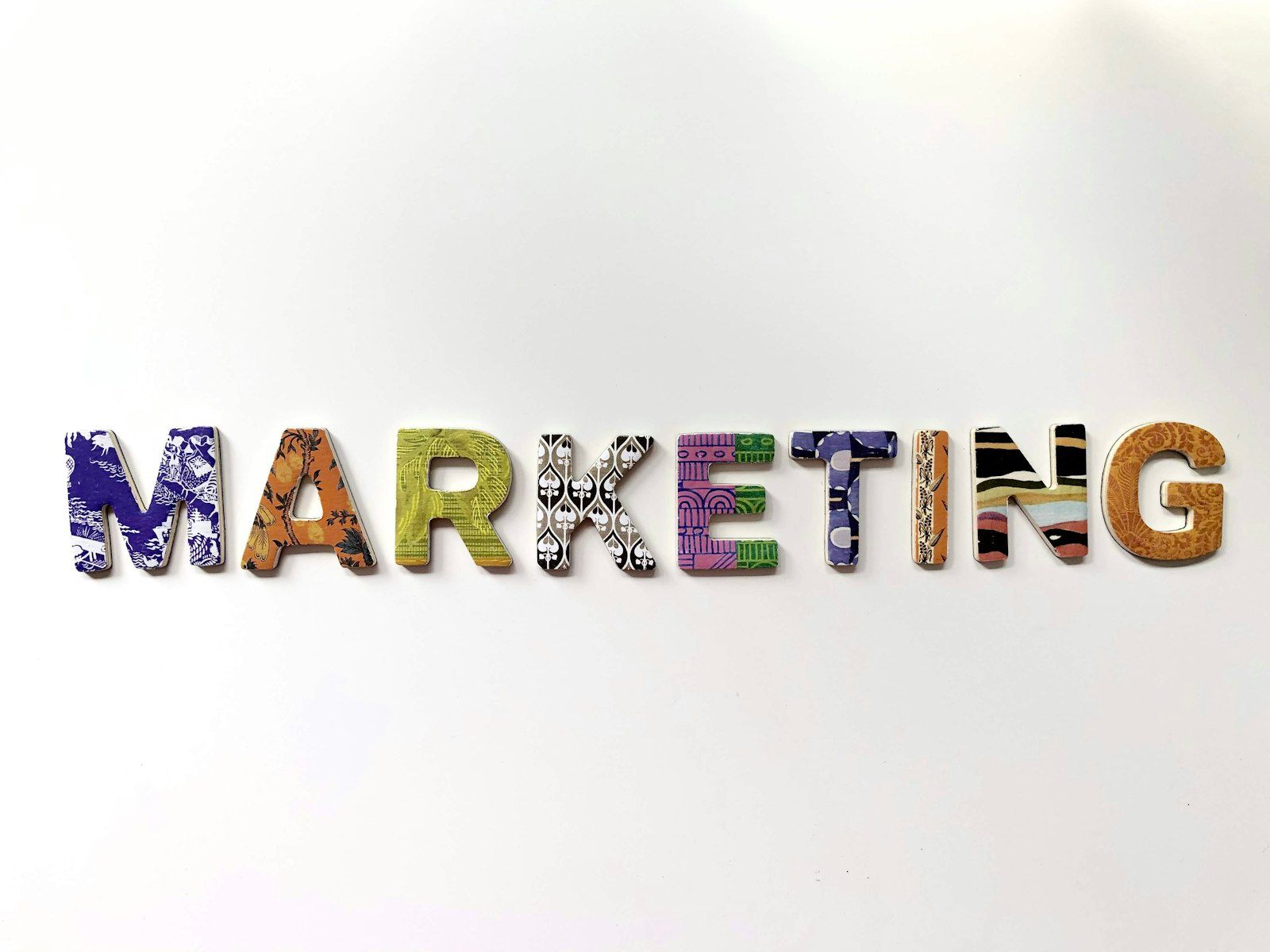 The image features the word 'MARKETING' constructed from multi-colored, patterned letters displayed on a white background. Each letter showcases a unique design, emphasizing creativity and diversity in marketing principles.