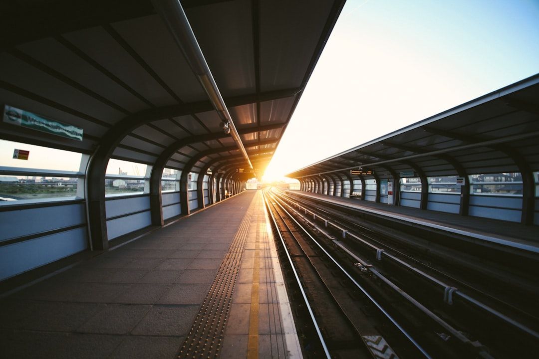 The image shows a train platform at sunset, with long shadows cast by the sun. The tracks are visible, leading away from the camera into the distance.