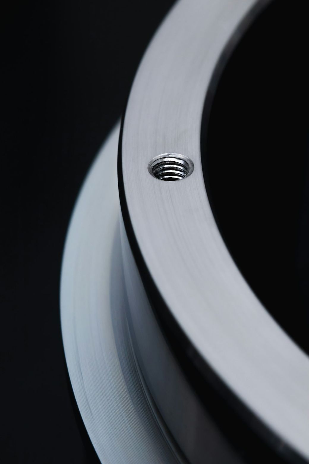 The image features a close-up view of a metallic component, showcasing a threaded hole and smooth, polished surfaces. The focus highlights the precision engineering of the part, set against a dark background. — Credit: Photo by Greg Rosenke on Unsplash
