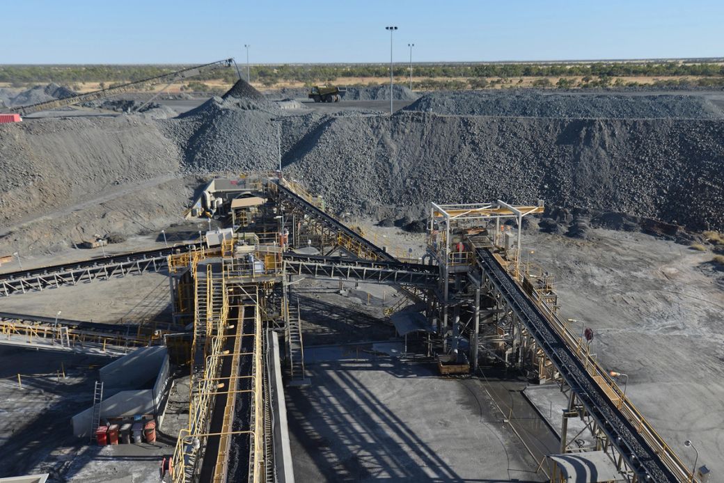 The image depicts an aerial view of a mining operation site with heavy machinery and conveyor systems in a rocky landscape. Large piles of extracted materials are visible in the background, showcasing an industrial environment.