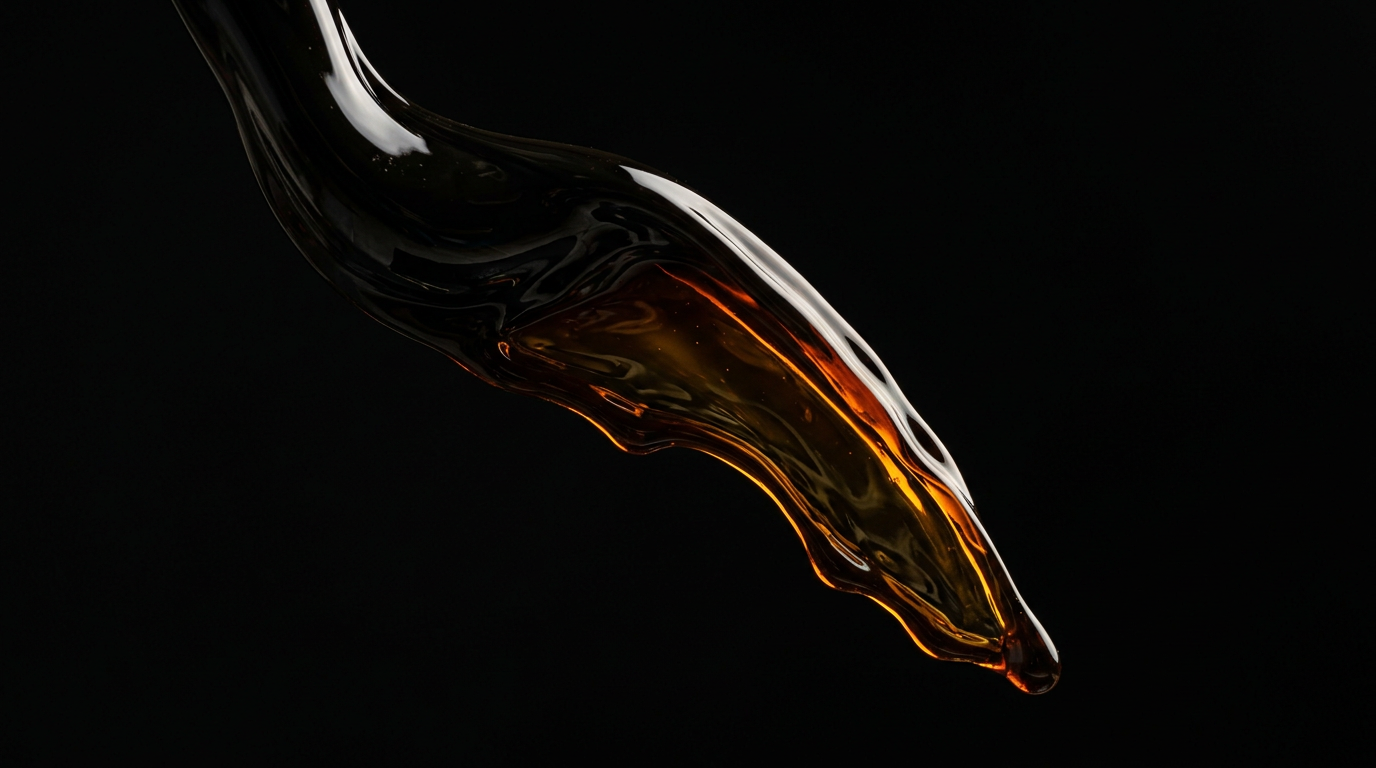 The image showcases a thick stream of crude oil flowing in slow motion against a pure black background. The liquid captures warm side light, revealing rich amber and treacle hues, forming a viscous ribbon that twists under its own weight, suspended mid-frame and emphasizing the raw nature of this valuable commodity.