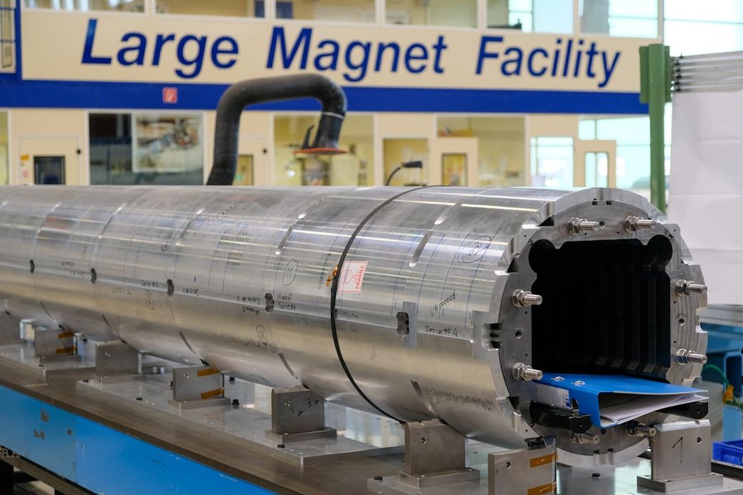 The image shows a large metal cylindrical component situated in a facility dedicated to magnet technology. It features a backdrop with the text 'Large Magnet Facility,' indicating its purpose and context. — Credit: Photo by Brandon Style on Unsplash