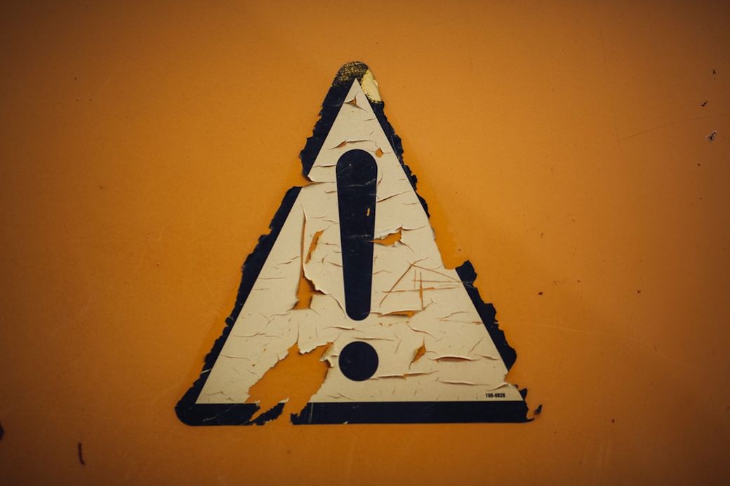 The image features a weathered yellow caution sign prominently displaying an exclamation mark. The surface of the sign is peeling and shows signs of wear, indicating it may have been exposed to the elements for some time. — Credit: Photo by Markus Spiske on Unsplash