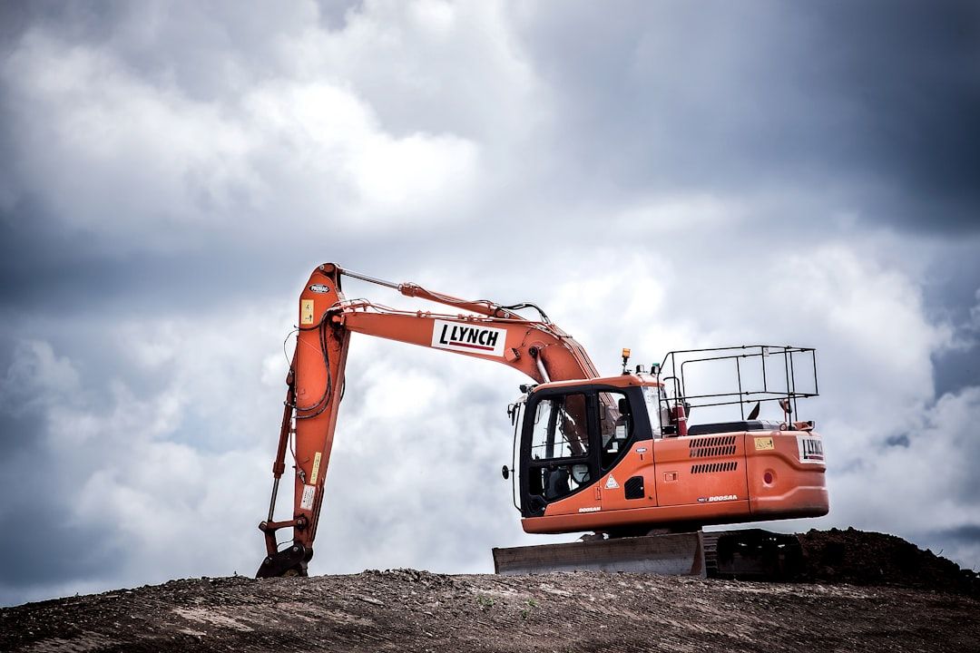 A bright orange excavator is prominently positioned on a construction site. The machine is actively engaged in earthmoving amidst a cloudy sky.