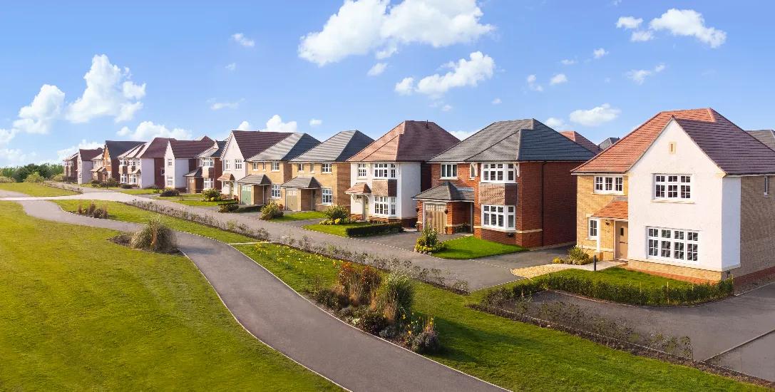 A residential area featuring a row of modern houses set against a clear blue sky. The well-maintained lawns and neat pathways indicate a planned community.