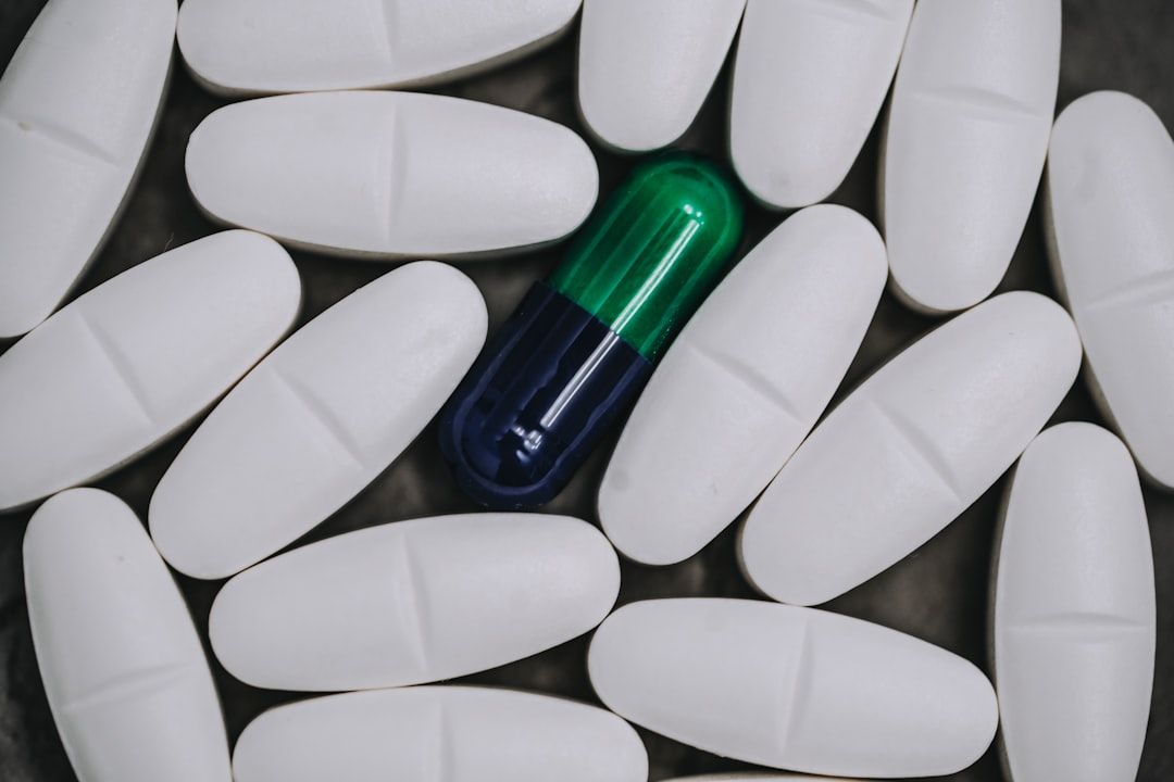 The image shows a collection of white capsules arranged in a circular pattern, surrounding a single blue and green capsule. The contrast highlights the distinctiveness of the colored capsule among the white ones.