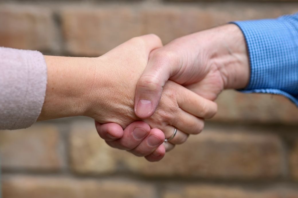 A close-up image of two hands engaged in a handshake, symbolizing agreement or partnership. The background features a textured stone wall, providing a neutral setting that emphasizes the handshake. — Credit: Photo by dlxmedia.hu on Unsplash