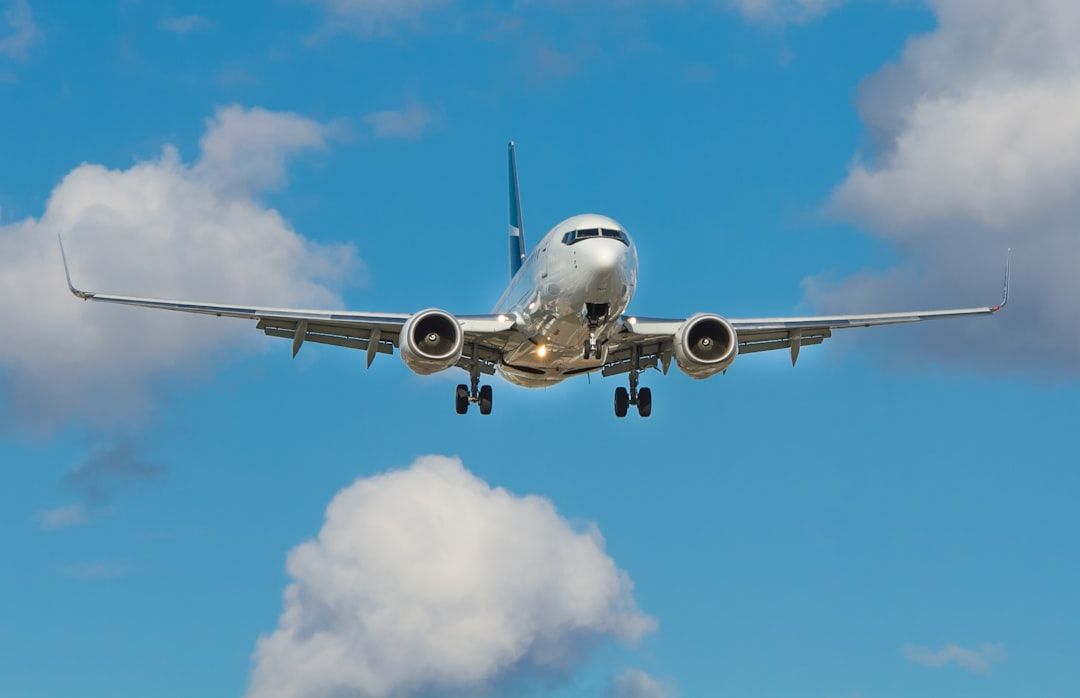A commercial airplane is approaching for landing against a backdrop of blue sky and scattered clouds. The plane, shown from a low angle, highlights its wingspan and landing gear.