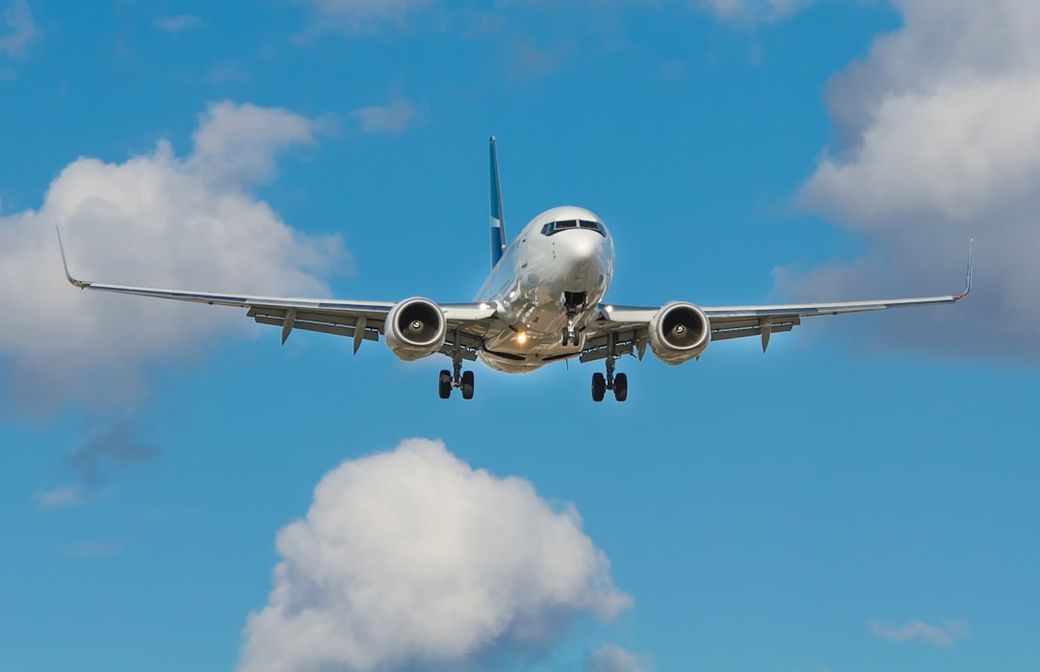 A commercial airplane is approaching for landing against a backdrop of blue sky and scattered clouds. The plane, shown from a low angle, highlights its wingspan and landing gear. — Credit: Photo by John McArthur on Unsplash
