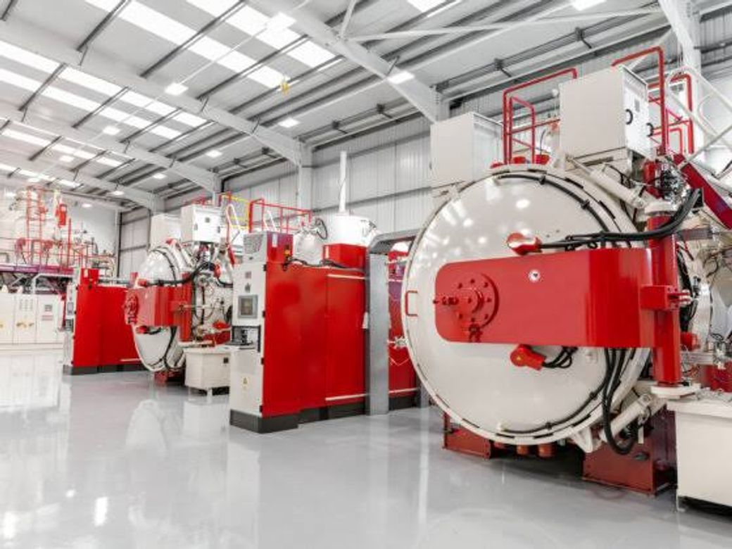 The image showcases a modern industrial facility featuring large red machinery and equipment. The spacious interior is well-lit with natural light coming through the overhead skylights.