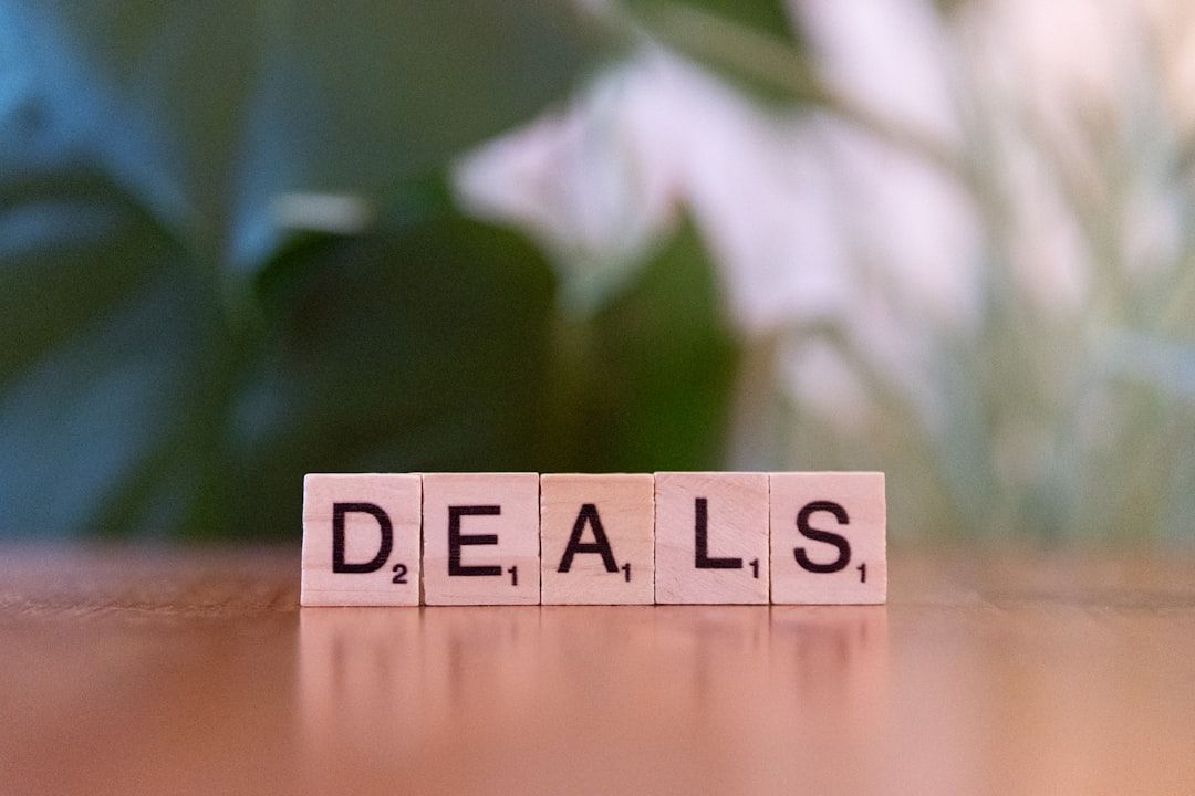 The image features Scrabble-style letter tiles arranged to spell the word 'DEALS'. The background consists of soft green foliage, creating a natural and inviting atmosphere.