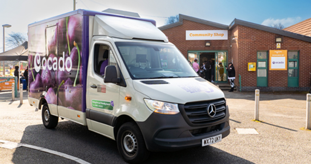 A delivery van from Ocado is parked outside a community shop. The building features a welcoming entrance with clear signage indicating its services.