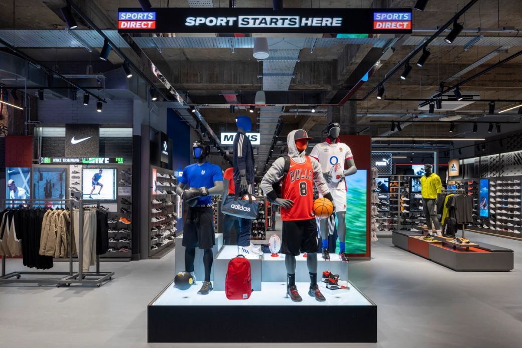 The image showcases a modern sports retail store interior featuring various athletic apparel and footwear. Mannequins are displayed in sports gear, highlighting brands like Adidas, with an emphasis on basketball and athletic performance.