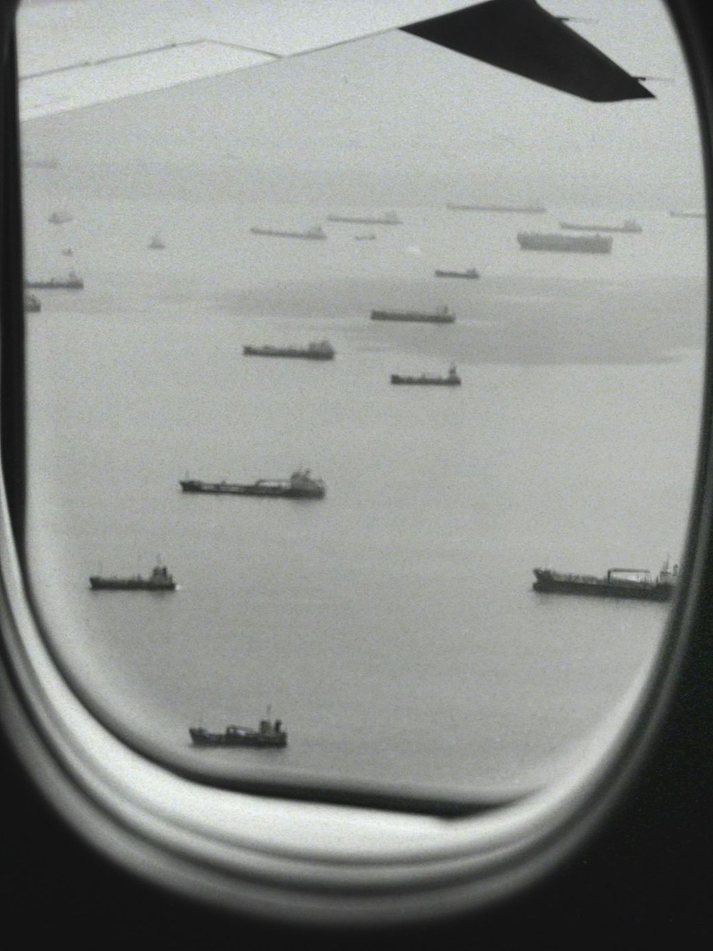This image captures a view from an airplane window, showcasing a maritime scene with several cargo ships scattered across the water. The monochromatic tone adds a vintage feel to the composition. — Credit: Photo by Tomás Robertson on Unsplash