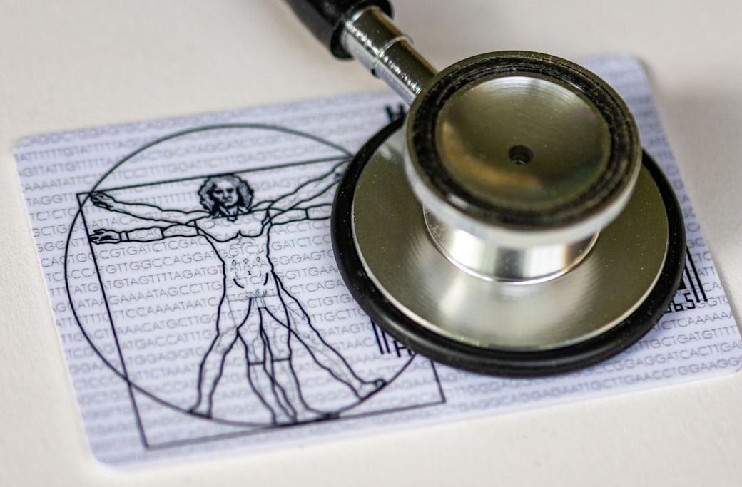 The image features a stethoscope resting on a card that showcases an artistic representation of the Vitruvian Man alongside DNA sequence text. This combination symbolizes the intersection of medicine and biology. — Credit: Photo by Marek Studzinski on Unsplash