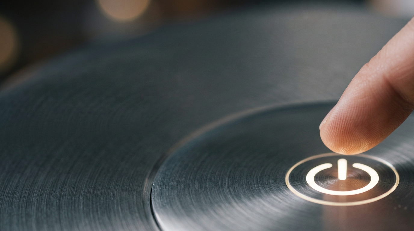 The image captures an abstract macro shot of a circular power button symbol backlit in soft white against a brushed aluminum surface. A fingertip hovers just above the symbol, illustrating the moment before activation, with a shallow depth of field highlighting the glowing symbol and the fine details of the metal.