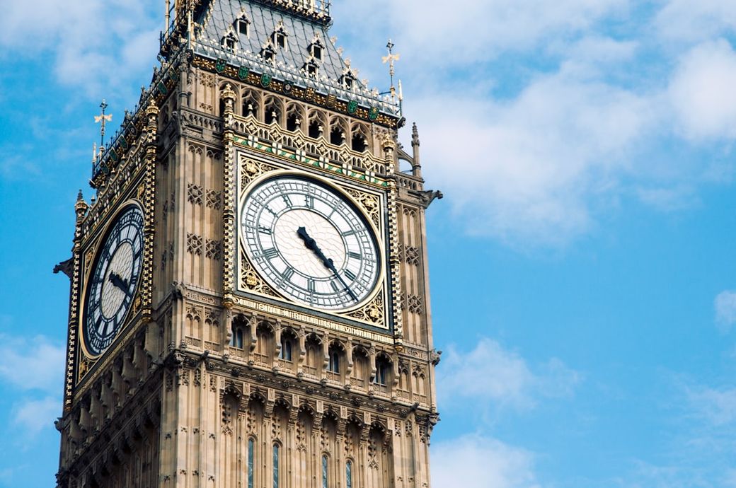 A close-up view of Big Ben, the iconic clock tower located at the north end of the Palace of Westminster in London. The clock displays Roman numerals and ornate detailing against a clear blue sky. — Credit: Photo by James Newcombe on Unsplash