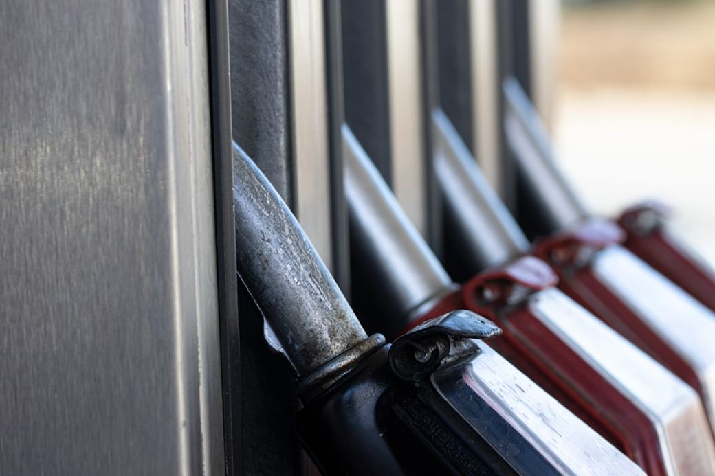 The image shows a close-up view of fuel pump nozzles at a gas station, highlighting the metallic nozzle ends with a focus on the detail and texture of the equipment. The background features blurred pump panels, emphasizing the fuel dispensing setting. — Credit: Photo by Marek Studzinski on Unsplash