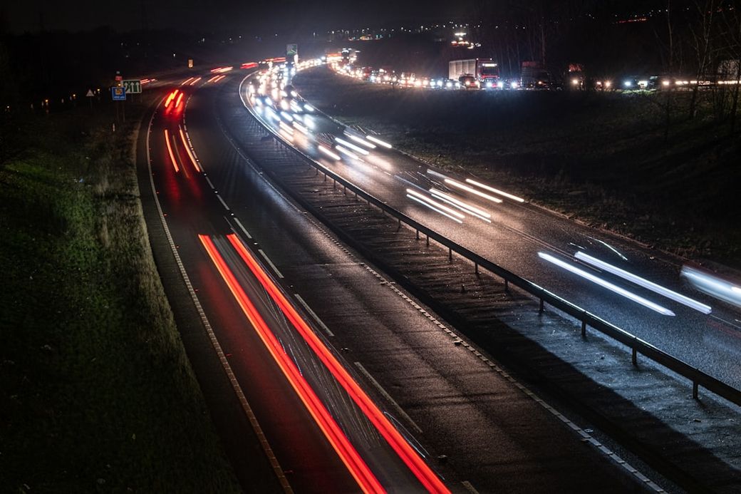 A night view of a busy highway showing streaks of car lights as vehicles travel in both directions. The image captures the movement of traffic with blurred lights, highlighting the bustling nature of nighttime driving. — Credit: Photo by Roger Bradshaw on Unsplash