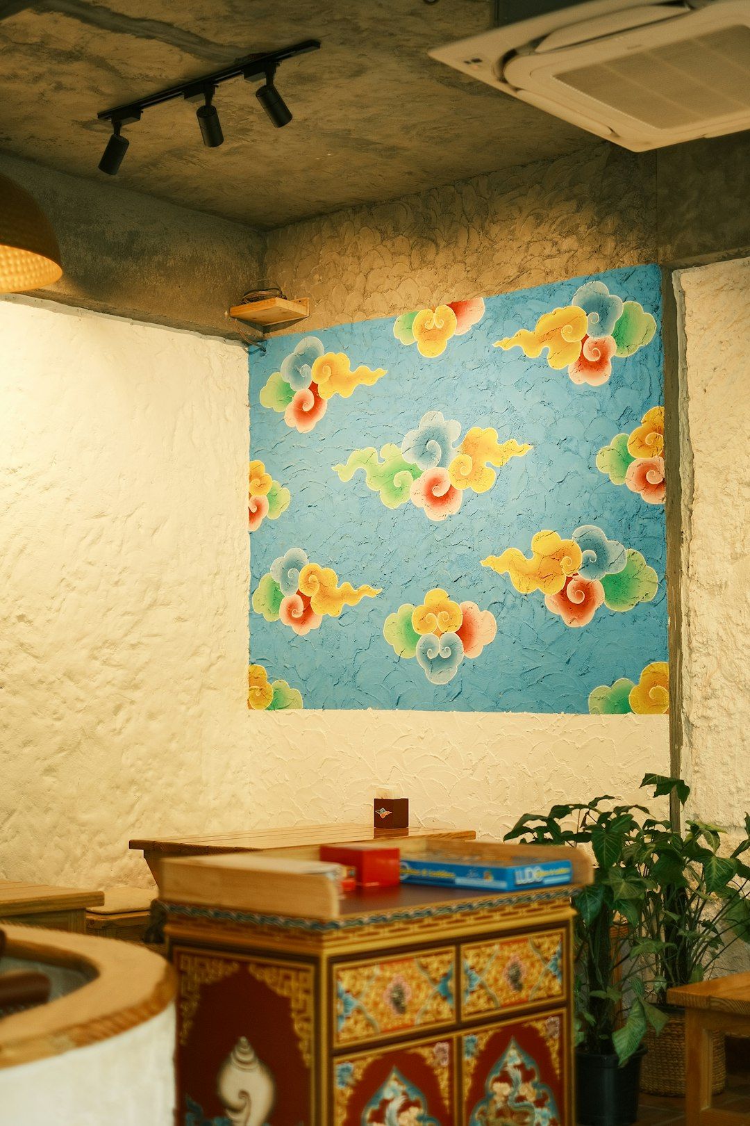 The image captures a cozy interior of a café featuring a vibrant wall adorned with colorful abstract cloud patterns. There is a wooden table and decorative elements that contribute to the warm atmosphere of the space.