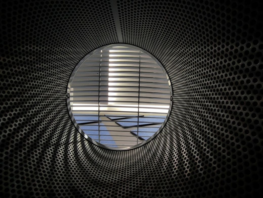 The image features a circular view from the inside of a metallic structure with a perforated pattern. Light filters through the openings, creating a dynamic interplay of shadows and reflections on the interior surface. — Credit: Photo by Brian Kairuz on Unsplash
